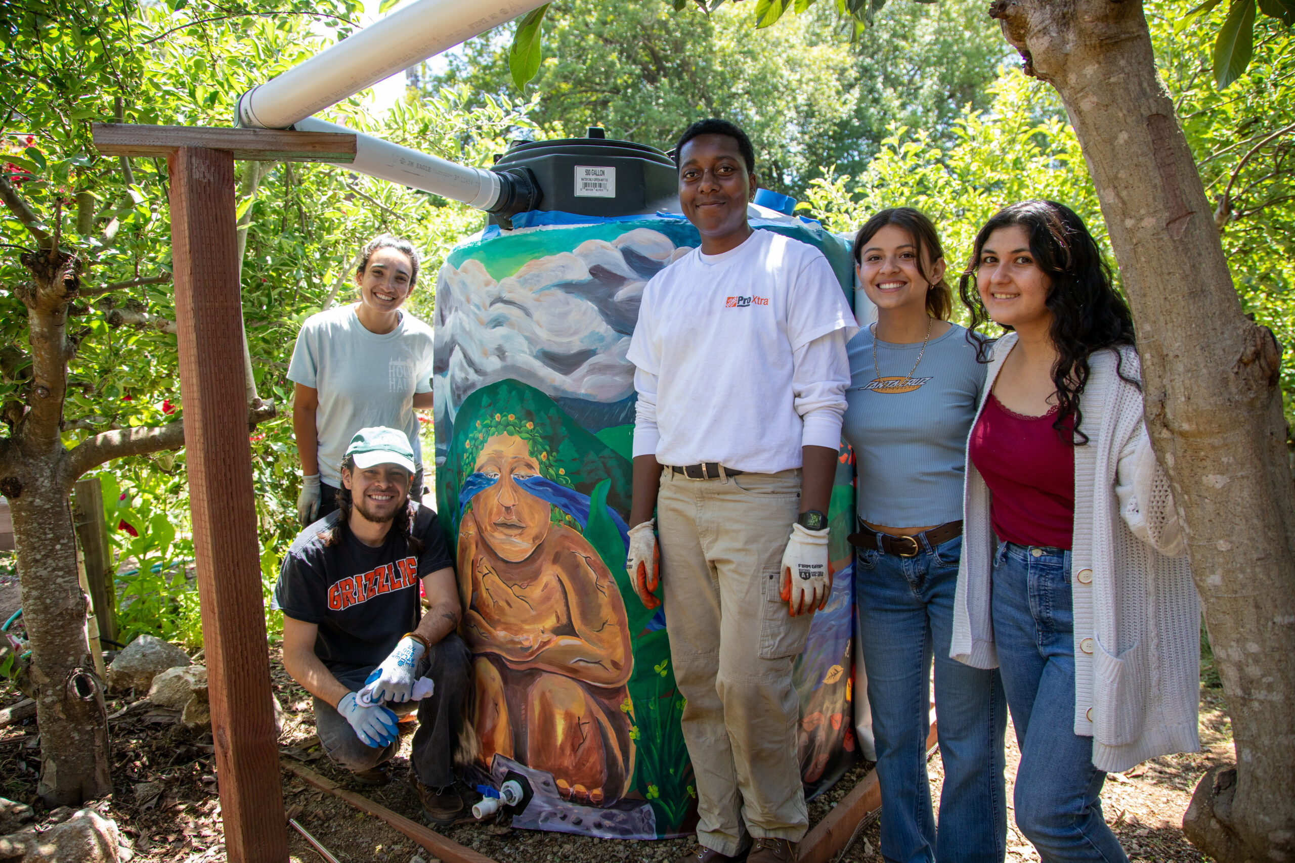 Students standing next to large water tank wrapped in a painted mural